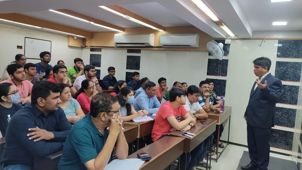 सूट पहने एक व्यक्ति कक्षा में छात्रों के समूह को व्याख्यान दे रहा है।